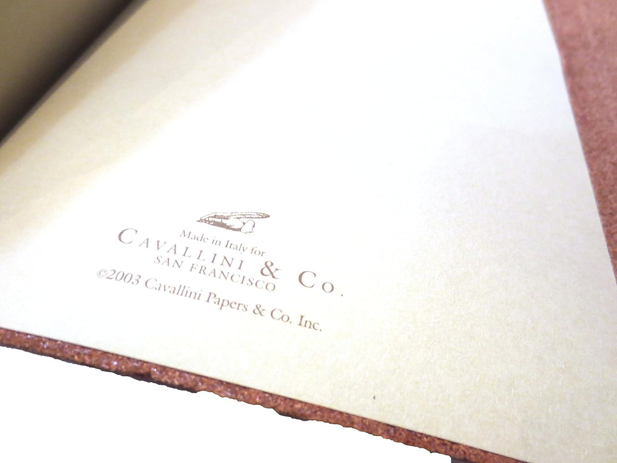 Close-up of a cream-colored paper insert printed with Cavallini &amp; Co. branding and copyright text, bordered by a textured reddish-brown material.
